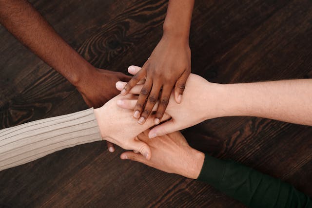 A number of crossed hands from people around the world, atop a table.
